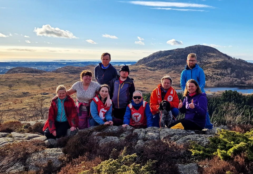 Gruppebilde på et fjell hvor 6 personer står sammen med 3 personer som har DNT-vest, og en hund