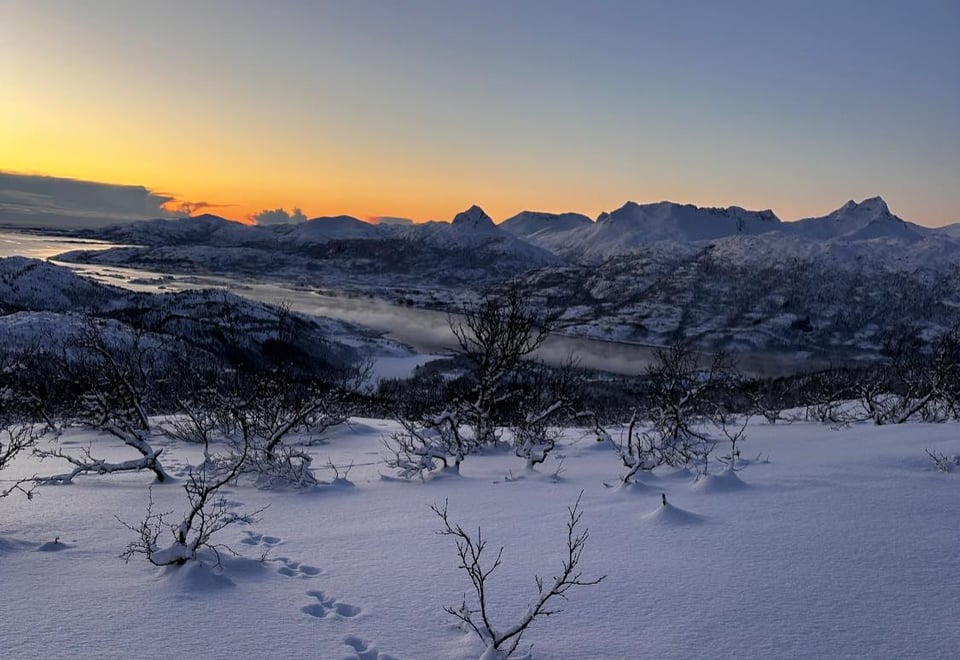 Sol under horisont bak snødekte fjell