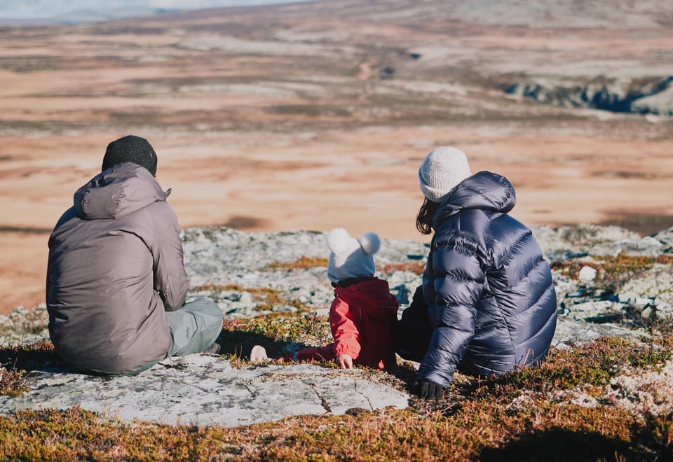 To voksne og et barn som sitter på en stein i fjellet. 