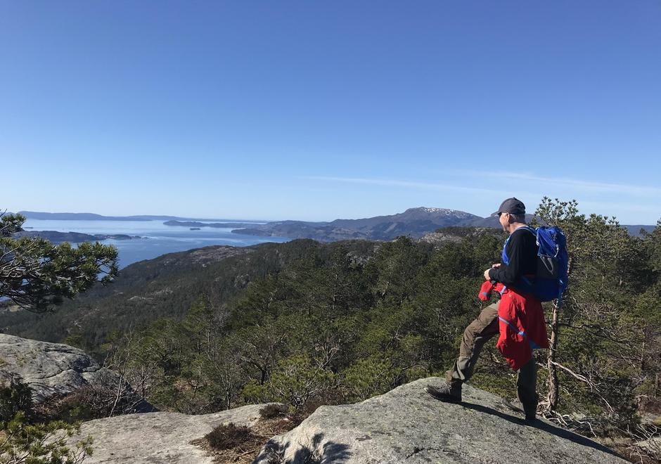 Ein turgåar på toppen av eit fjell med utsikt mot fjord og andre fjell og toppar i sol og blå himmel