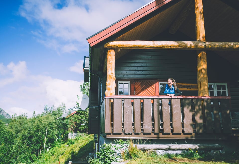 dame står på terrasse i fjellhytte omringet av grønne omgivelser