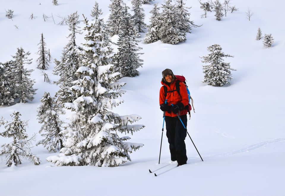 Kvinne i rød jakke står i hvitt snøkledd landskap med ski på beina.