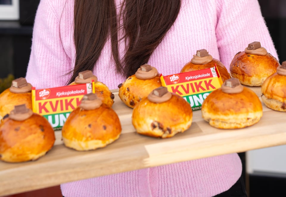 en person i rosa genser holder ei trefjøl med masse boller oppå. Det ligger også et par kvikk lunsj-sjokoladet på fjøla. 