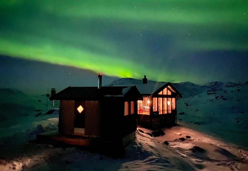 Hytte på snødekt fell opplyst av nordlyset