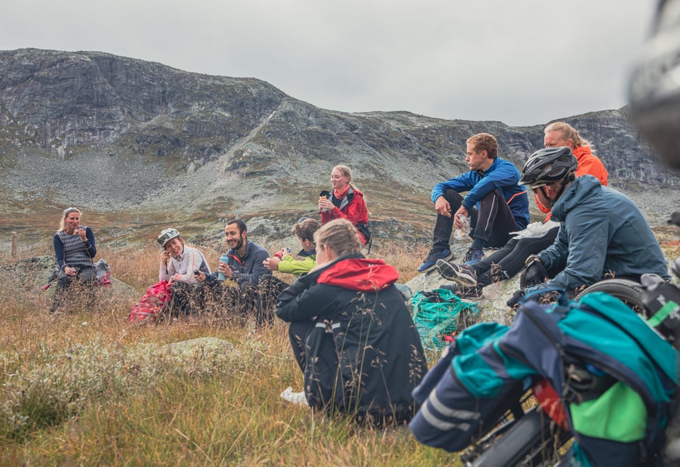 En gruppe ungdommer som har matpause, sitter på steiner i fjellet, som sykler Rallarvegen