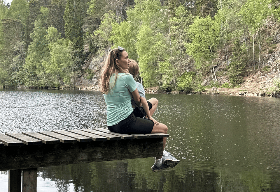 en mor og et barn på en bryggekant ved et skogsvann