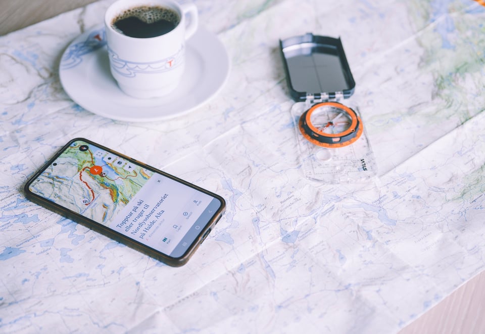 bilde av en telefon som ligger oppå et karty på et bord. ved siden av mobilen ligger det et kompass