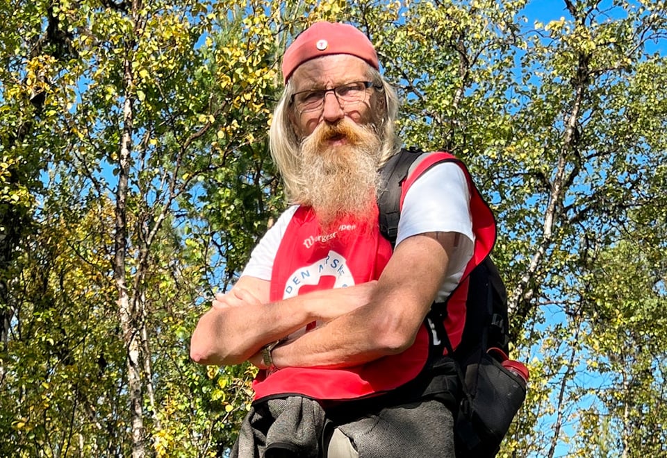 Mann med rød DNT-vest på tur i skogen. Foto.