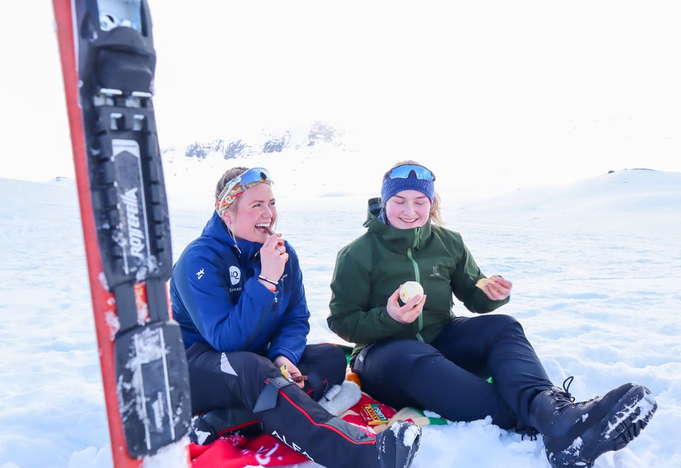 To damer sitter i snøen og spiser appelsin