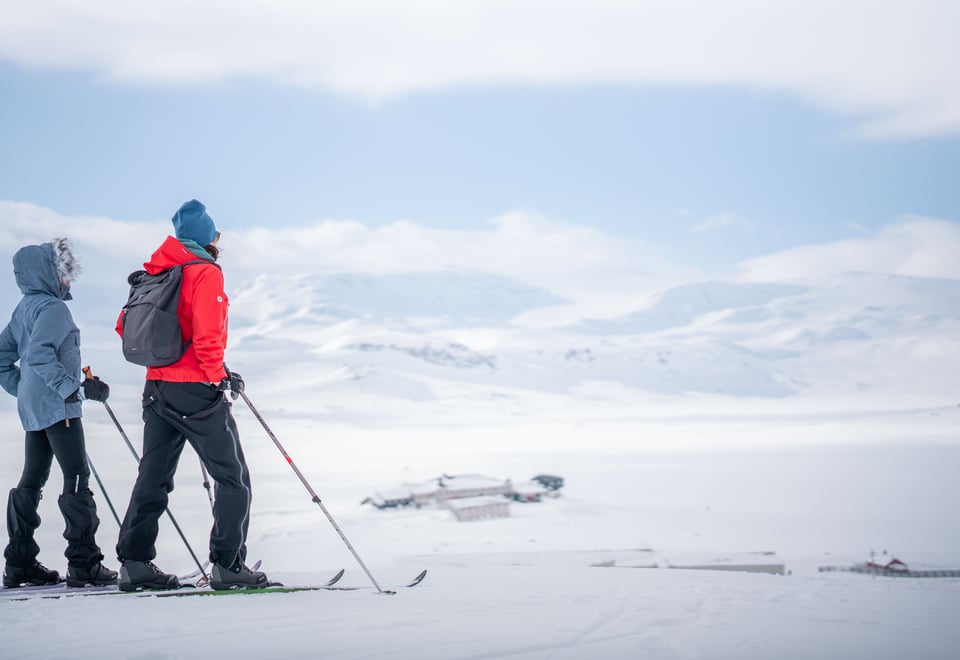 to personer på ski som ser utover Finsehytta og Finsevannet mot Hardangerjøkulen