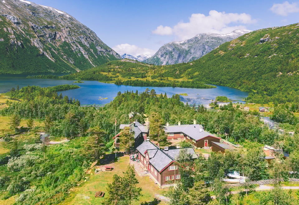hyttetun med flere hytter blant frodig fjellterreng med et stort fjellvann i sikte