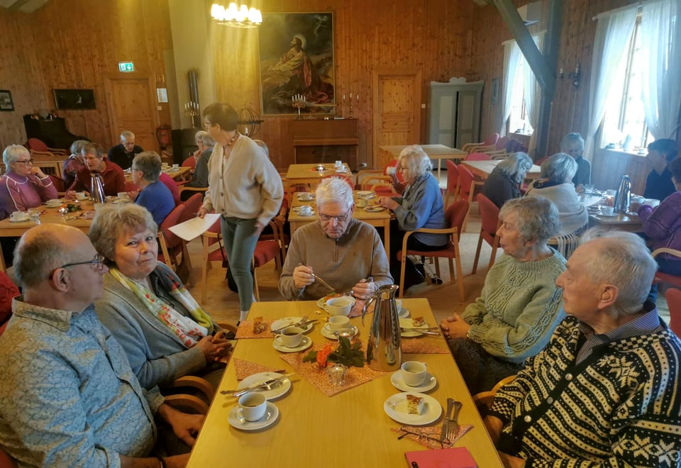 En gruppe eldre mennesker sitter rundt et bord med mat og drikke.