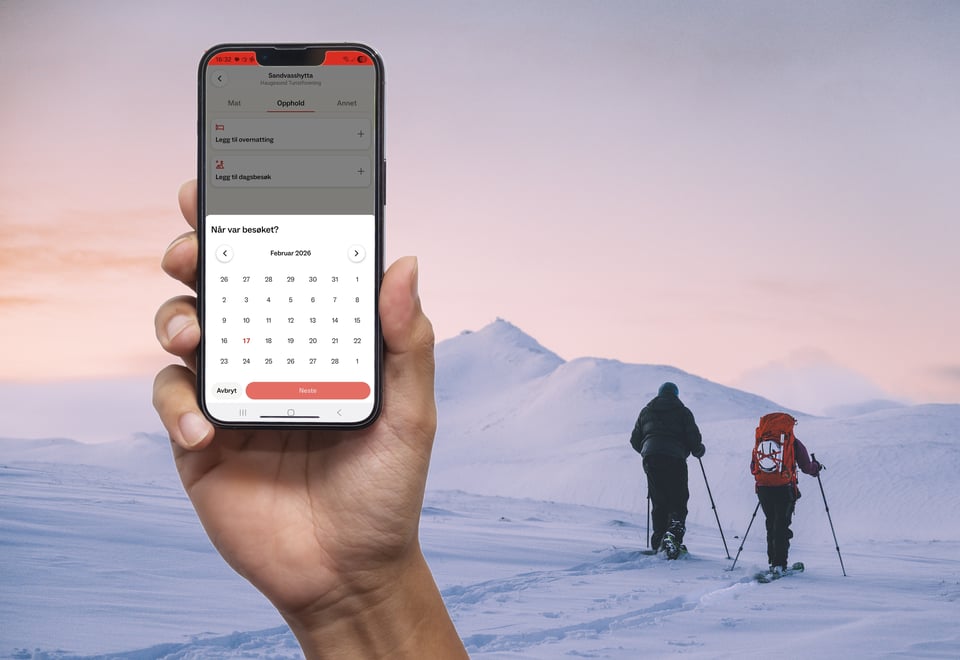 Hånd med mobil foran folk som går på ski i vinterlandskap