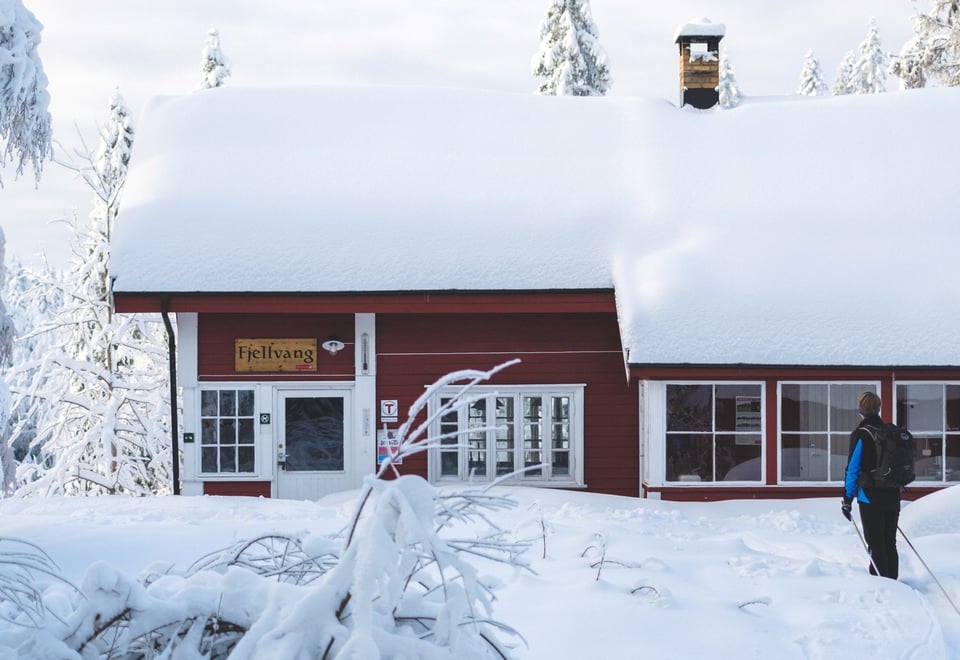 Mann foran en rødmalt hytte med mye snø på taket