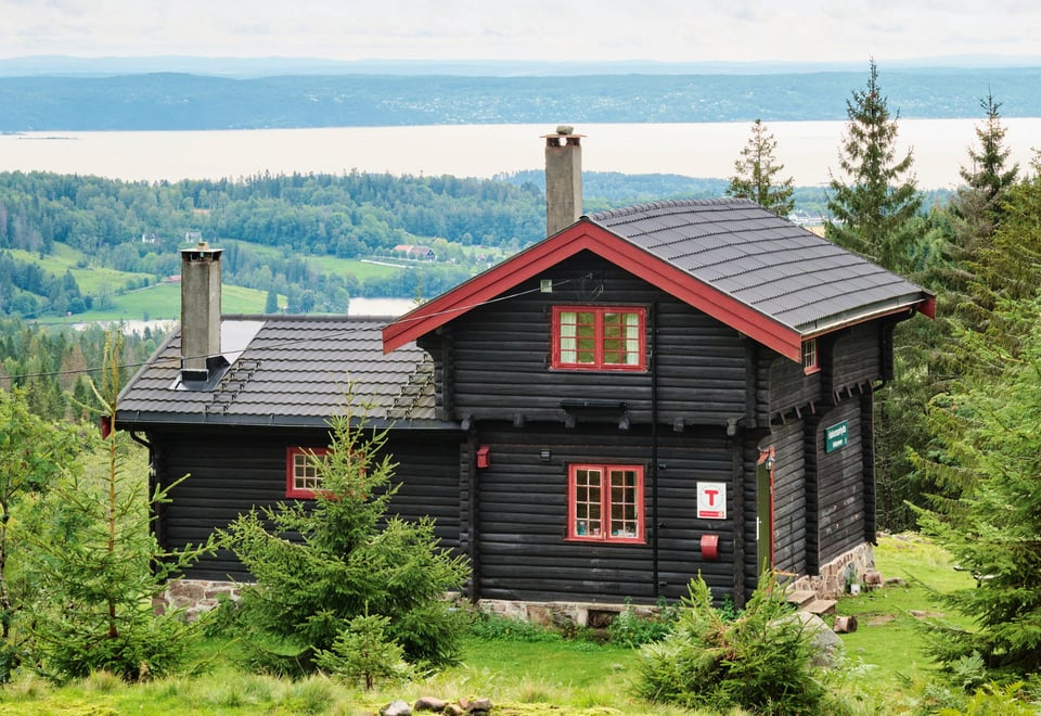 Svartmalt hytte med rødkarmer og fint utsikt mot Oslofjorden i bakgrunnen