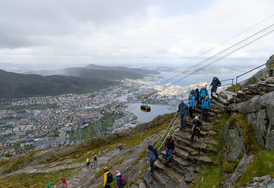 Mange turgåere går ned en steintrapp med utsikt over Bergen i bakgrunnen.