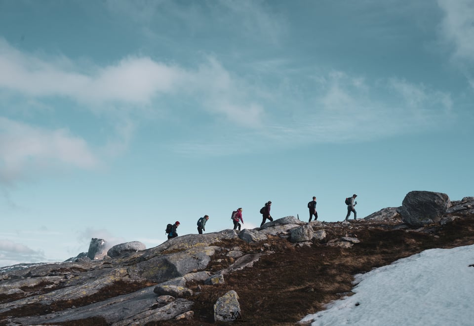 Seks ungdommer vises mot horisonten mens de går oppover ei fjellside