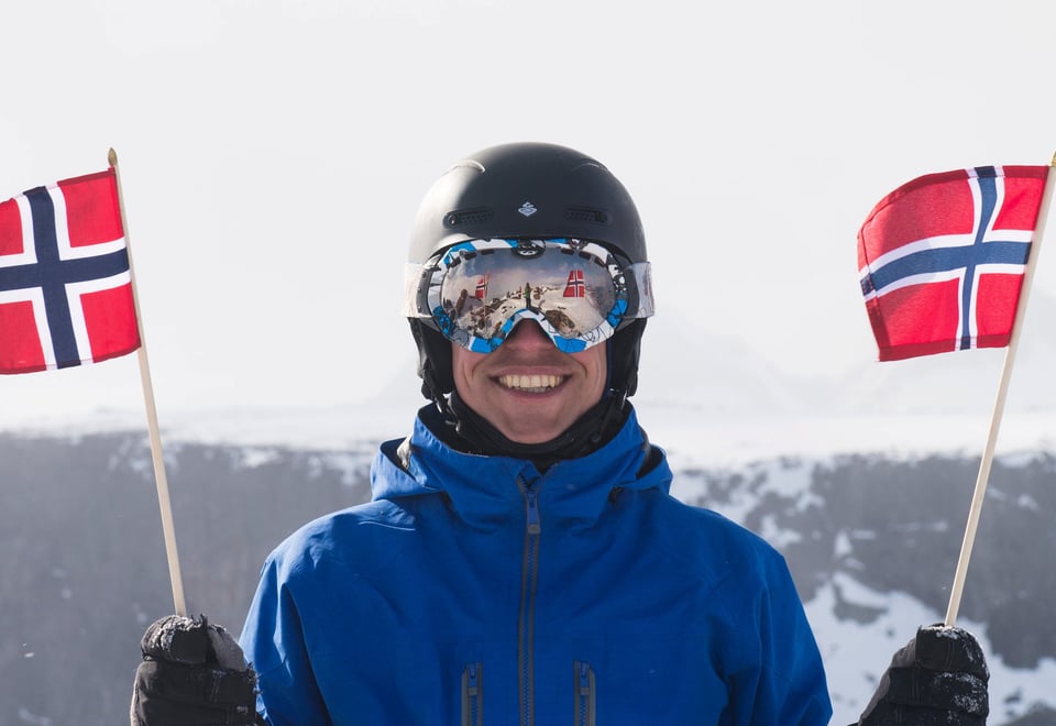 Flagging på Rasletind, en smilende fyr med skibriller og et norsk flagg i hver hånd.