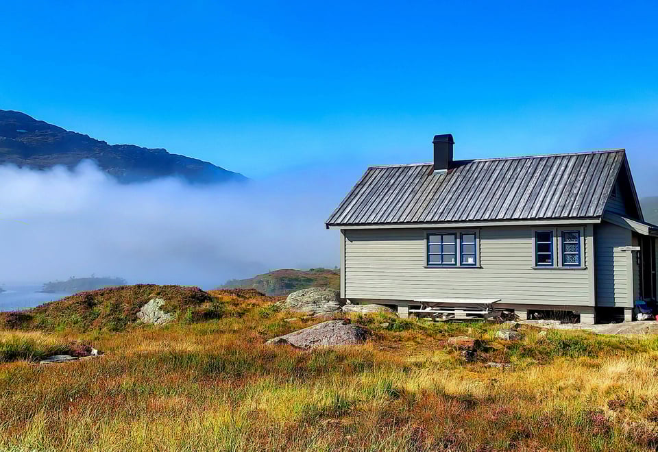 En hytte på fjellet med blå himmel og skodde. Foto.