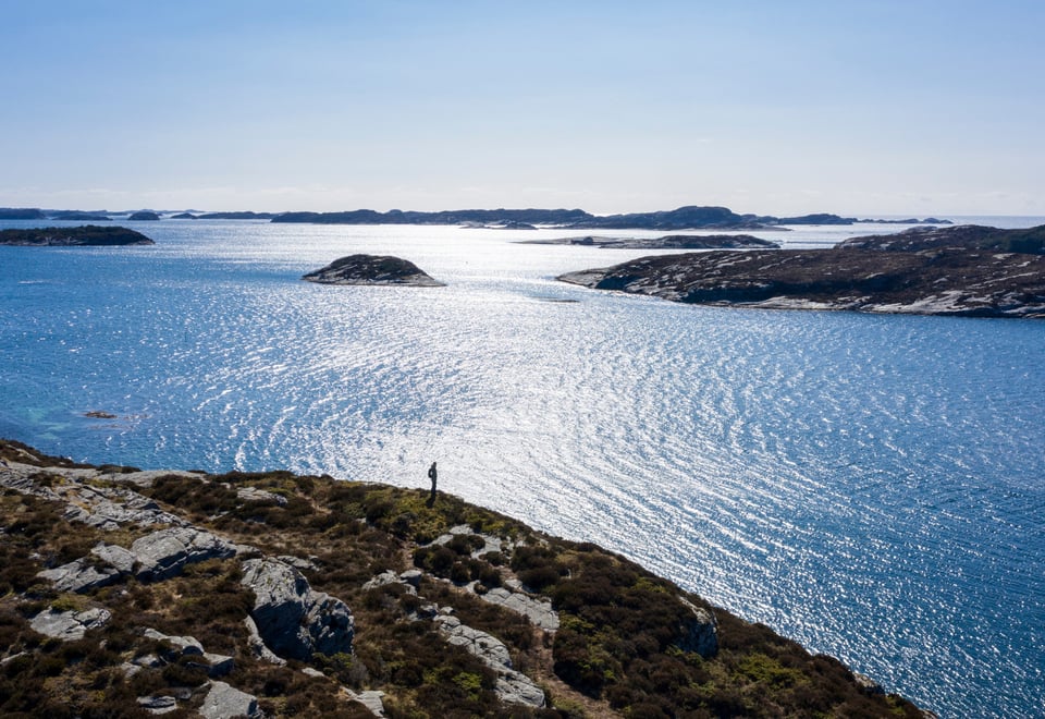 Person på tur langs klipper ute i havgapet. Sol og sjø. Foto