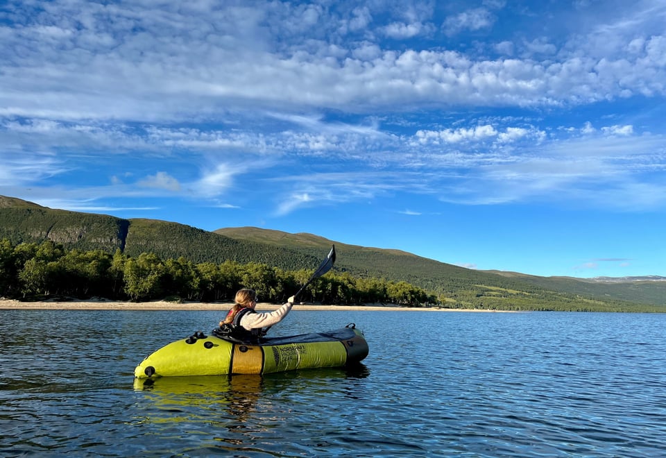 En person i en packraft padler på en innsjø om sommeren