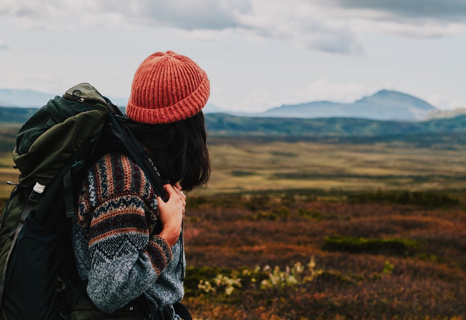 Person med sekk og oransje lue som ser utover fjellet
