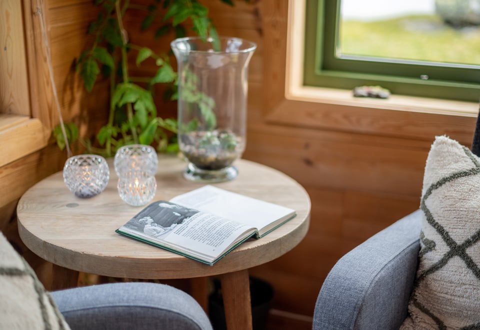 Nærbilde av en bok og en lyslykt som er plassert på et bord i stuen av hytta.