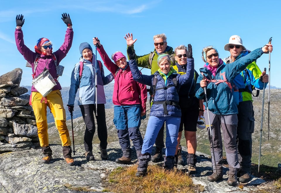 Gjeng glade turgåere med hendene i været på toppen av et fjell.