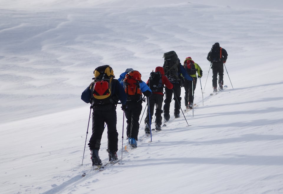 Toppturgåere i tog oppover gjennom snødekt landskap. 