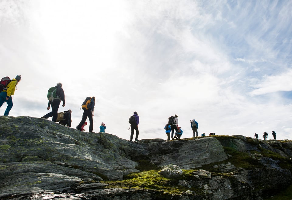 Mennesket på tur over en fjellrygg. Lettskyet og motlys. Foto