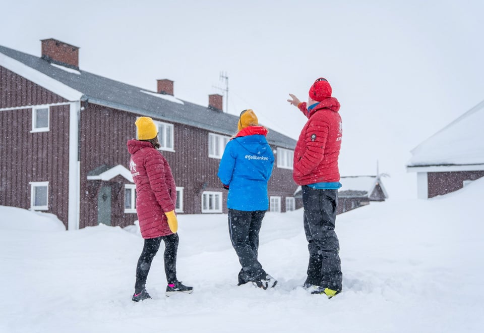 Bilde av tre personer som står foran DNT hytta Glitterheim. Vinteren 2023.