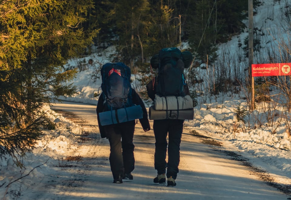 To personer med sekk som går tur på en grusvei dekket av snø