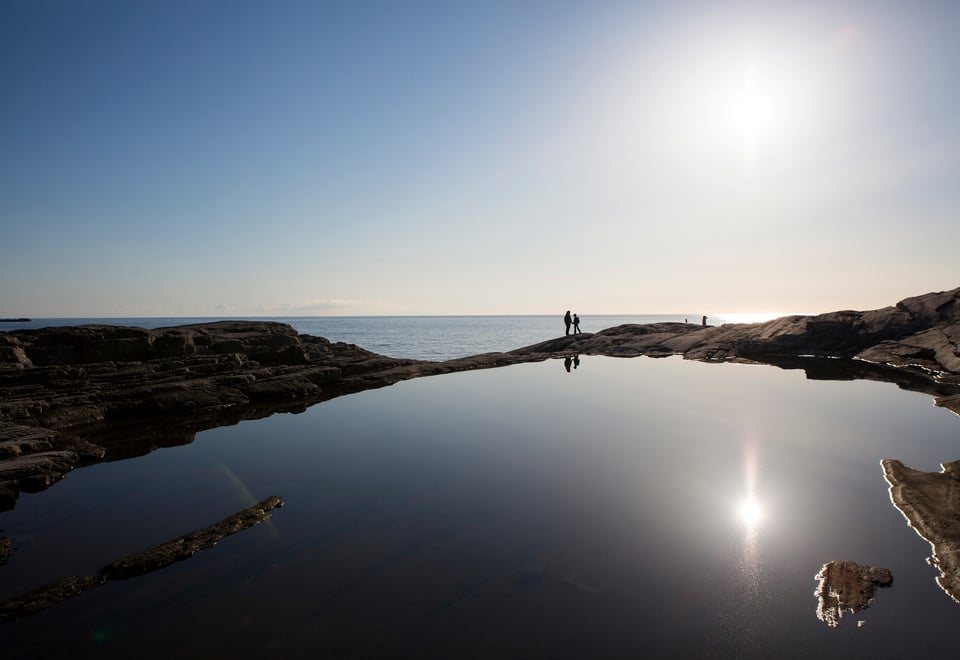 To personer går langs blikkstille kulp med solnedgang i havgapet.