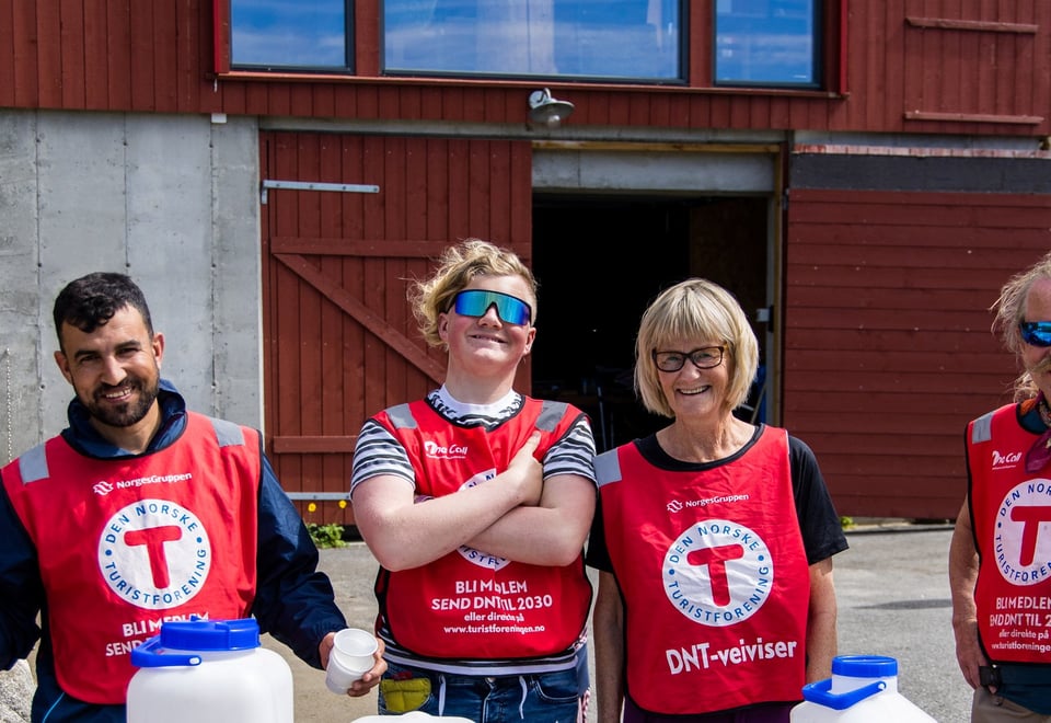 Smilende mennesker i røde vester med rød T på hvit bakgrunn smiler mot kamera 