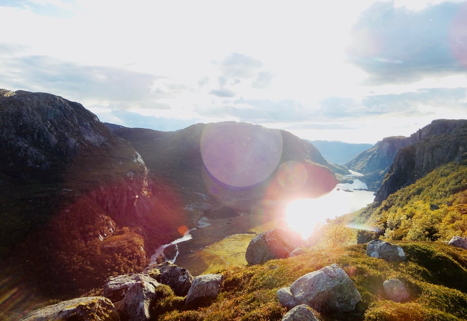 Solen som skinner mot steiner, gress, fjell og vann