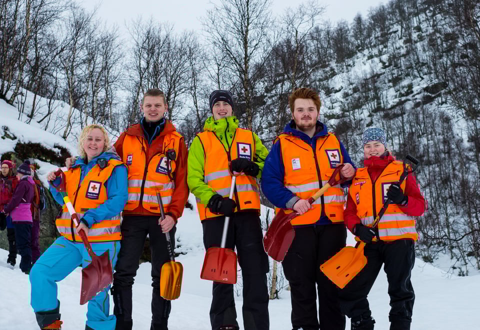 Fem personer med oransje vester og hver sin spade står i snøen og smiler