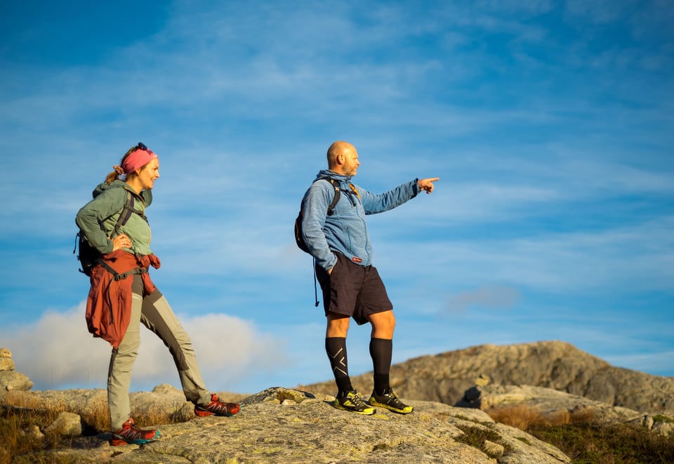 To personer står på et fjel og speider utover. Han ene peker