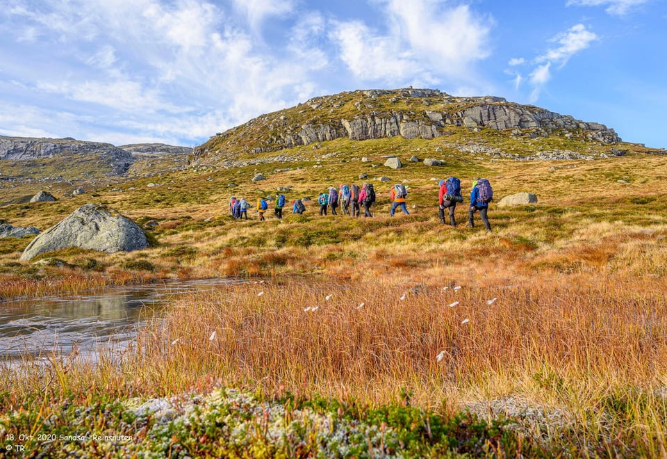 En gruppe med mennesker som går innover fjellheimen med tursekk