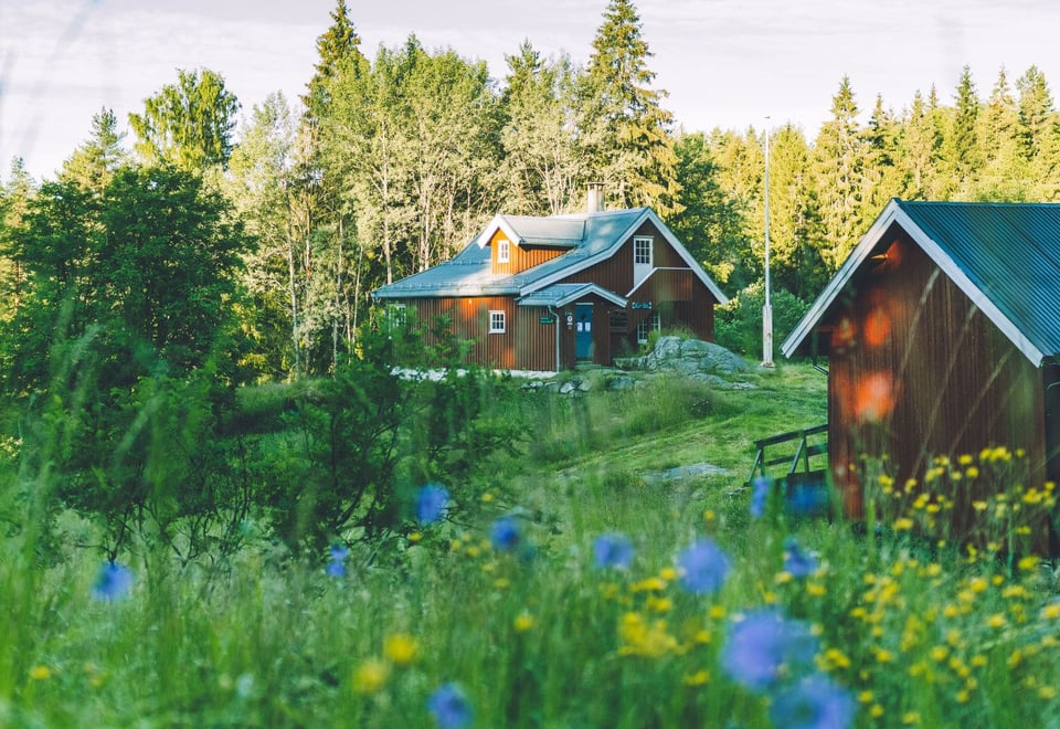 Rødt hus med uthus i vakker blomstereng