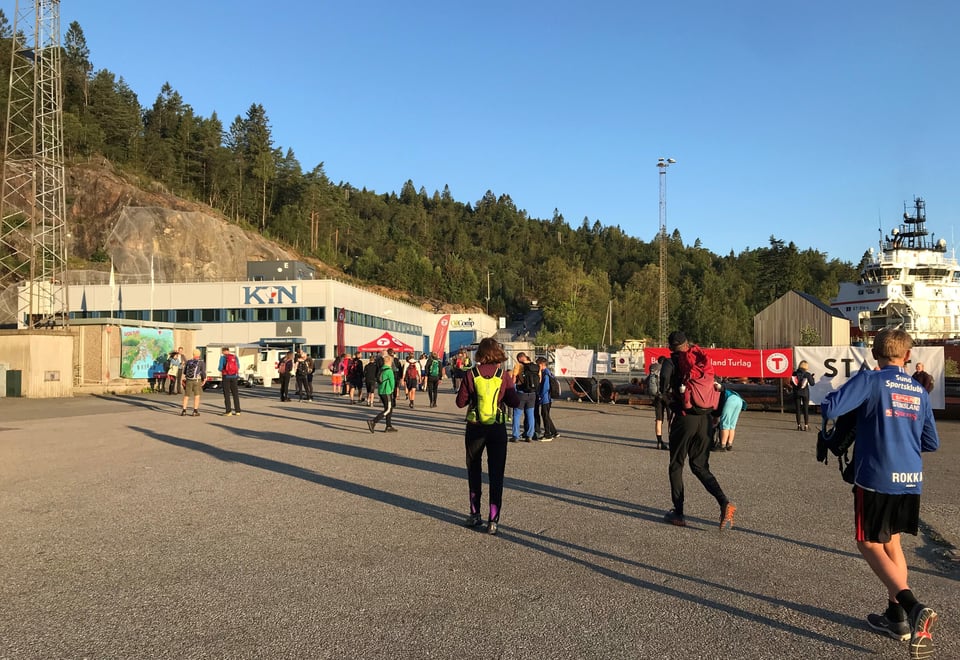 Folk går mot startområder på 7-fjellsturen en tidlig, solfylt morgenstund.