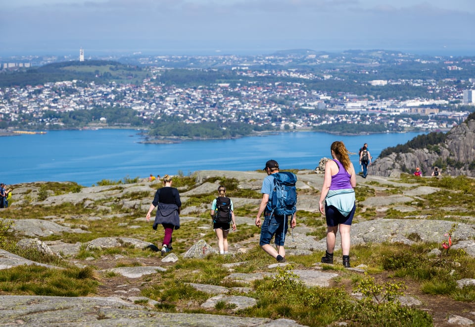 Fire voksne er på tur ned fra et fjell. Sjø og by i bakgrunn