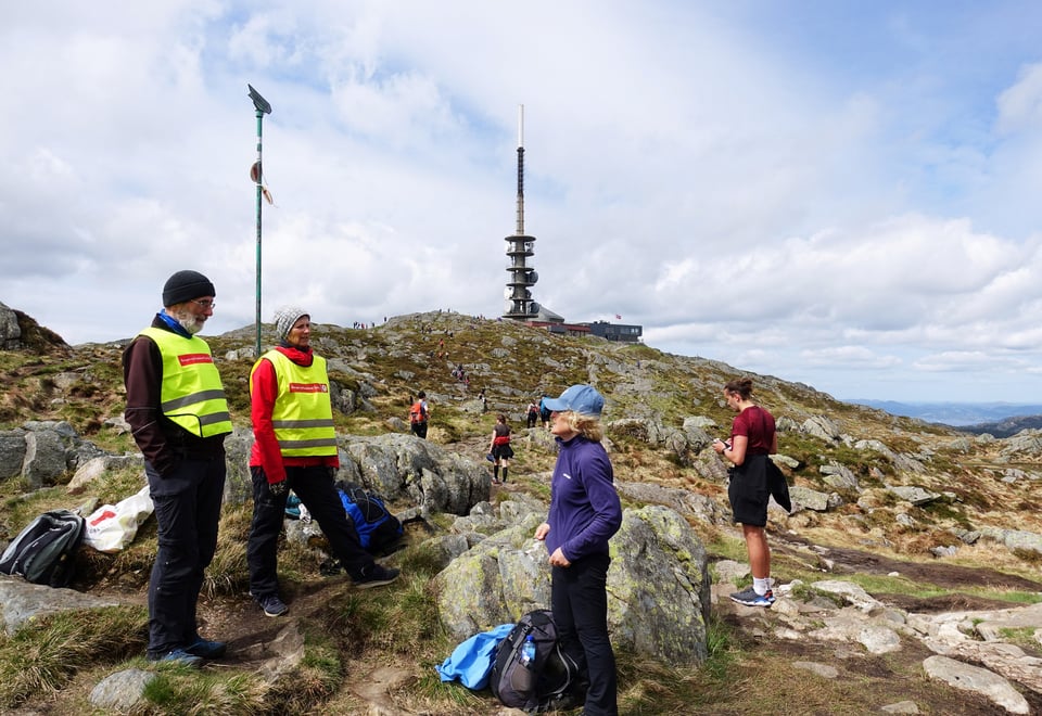 To friviilige står på en fjelltopp og tar i mot turgåere.