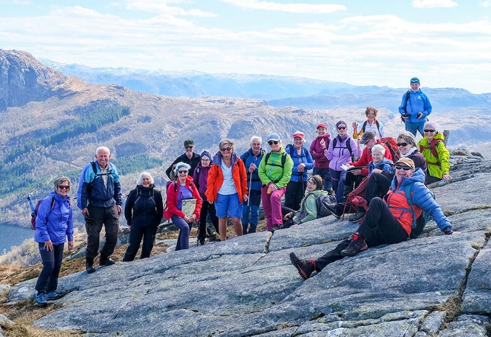 En stor turgruppe med mennesker i fargerike klær som er avbildet på en topptur i fjellet.