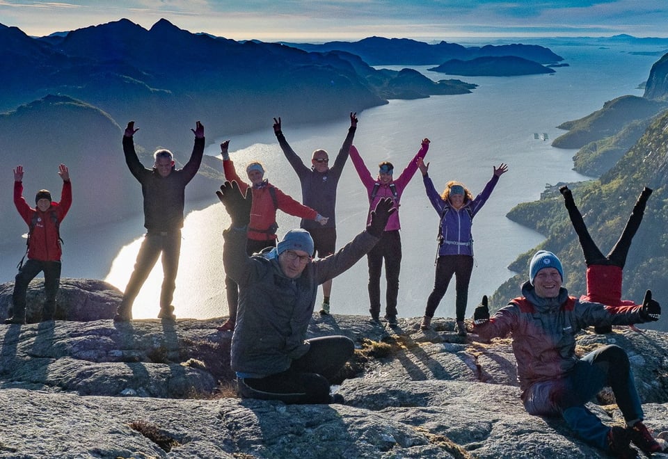 Mennesker på en fjelltopp som rekker hendene i været.