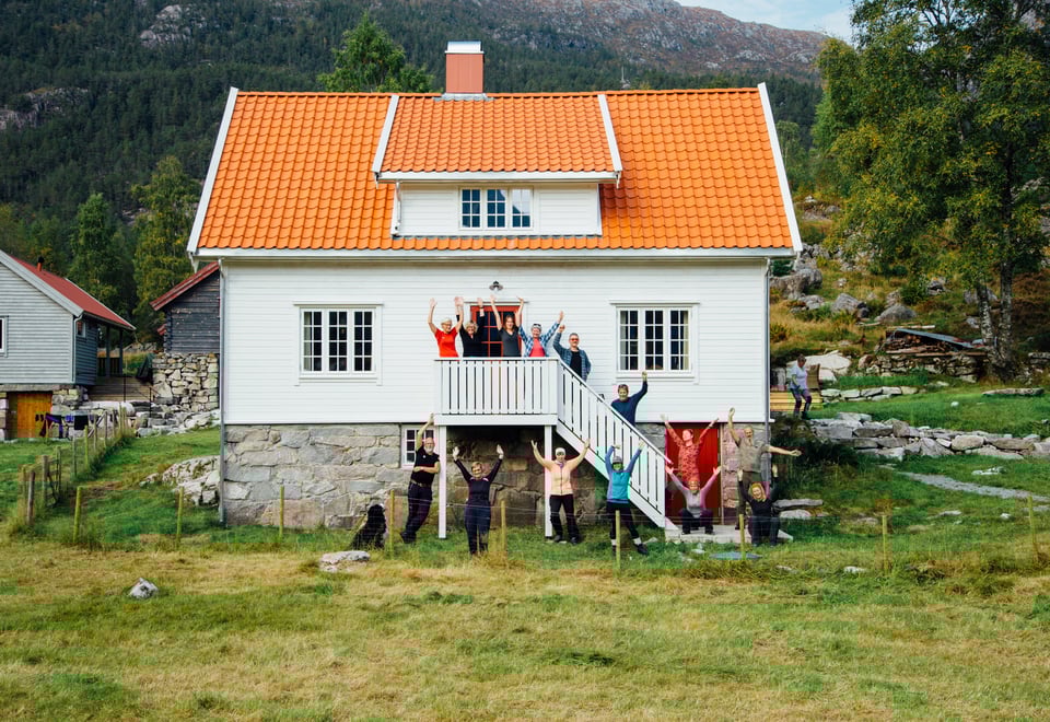 Flere mennesker står foran et hvitt hus og holder hendene i været.