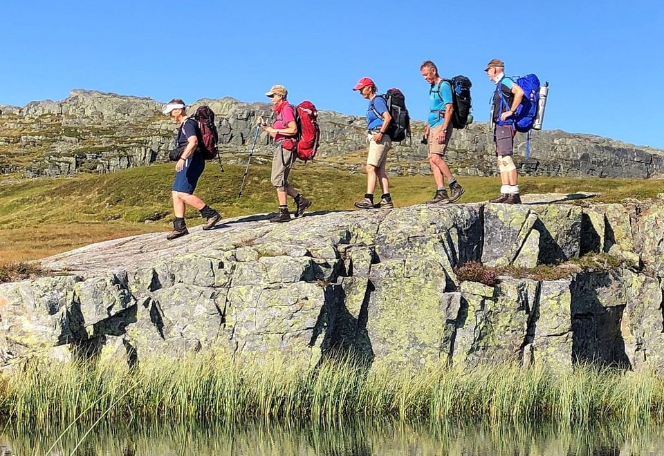 Fem personer som går over et berg, speilbilde i vannet nedenfor.