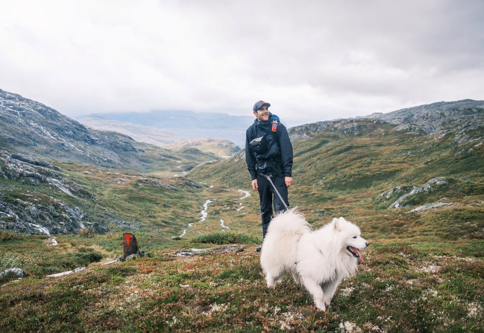 Mann med svarte turklær og caps står sammen med stor hvit hund på fjellet