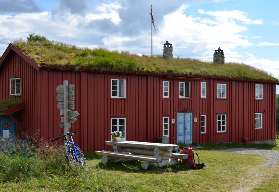 Blå himmel, grønt gress og rød hytte med torvtak
