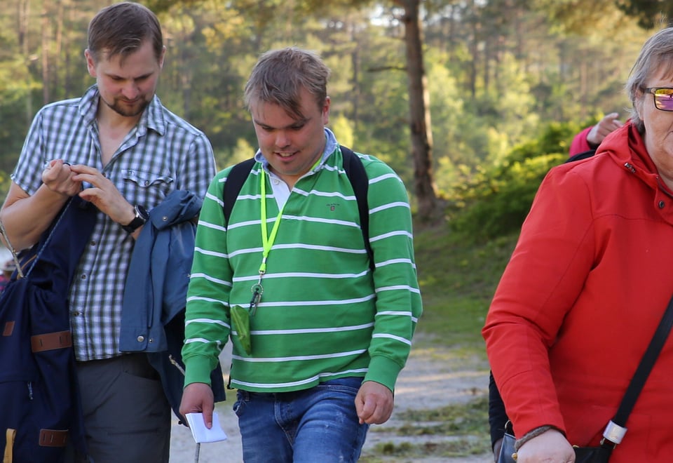 En liten gruppe mennesker går ved siden av hverandre langs et vann i skogen