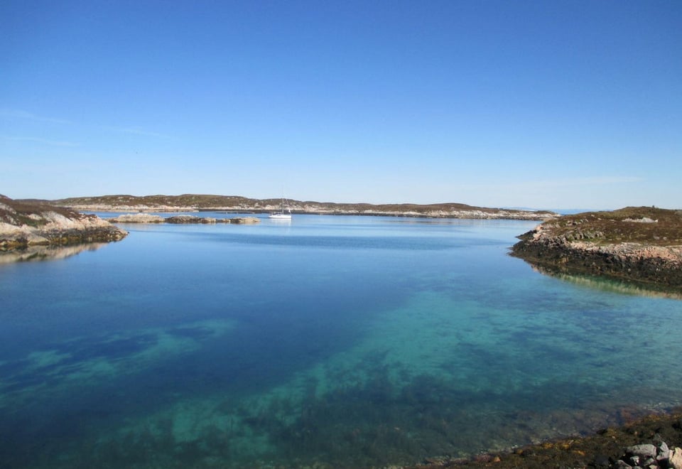 Utsikt over fjord eller innsjø, med noen få landbiter synlig til venste og i høyre hjørne, og videre ut i bakgrunnen. Skyfri himmel.